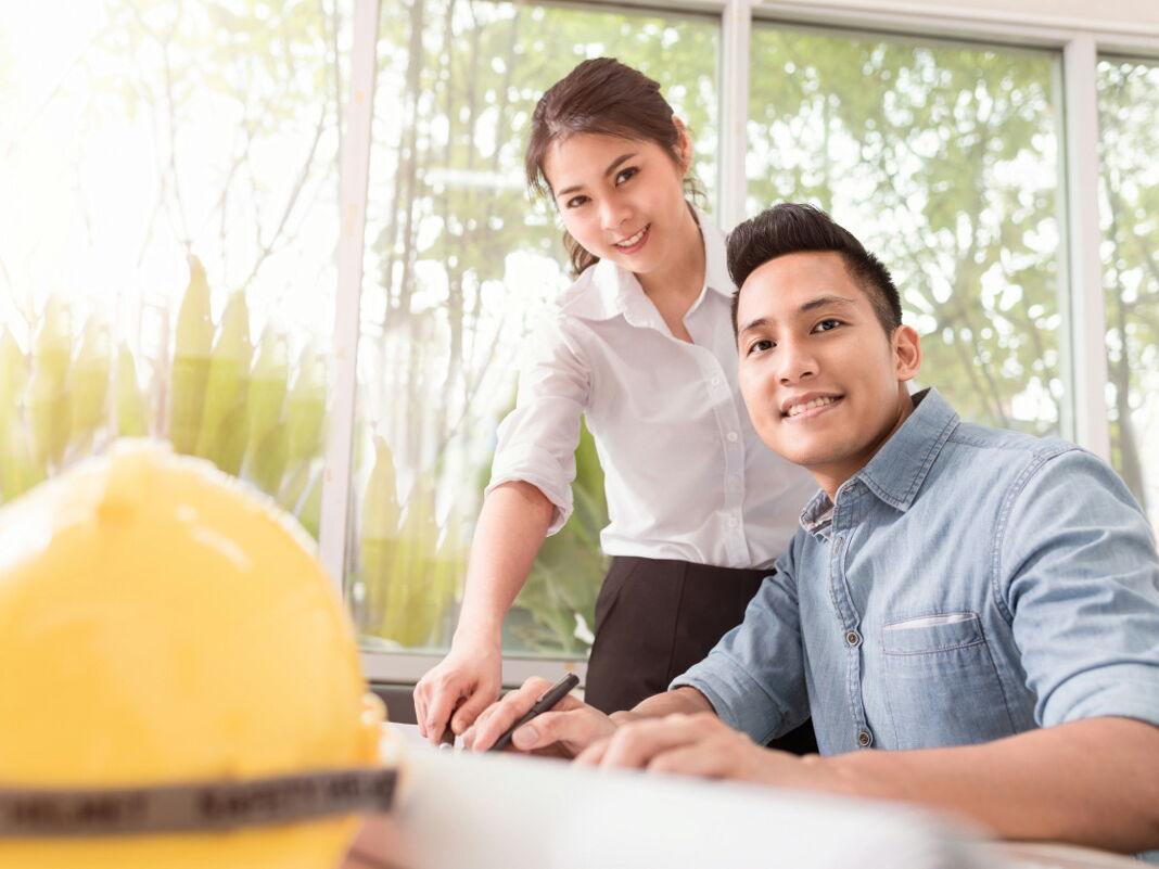 Engineer asia man and woman discussing about building plan for construction at job site, working on desk.
